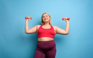 Fat girl does gym at home. satisfied expression. Cyan background photo