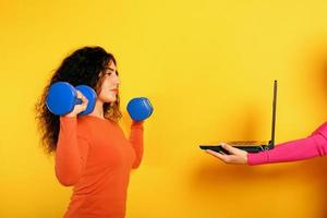 Girl with handlebars ready to start the gym online with a computer. yellow background photo