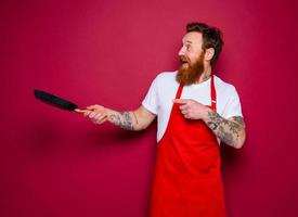 amazed chef with beard and red apron cooks with pan photo