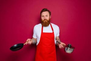 doubter chef with beard and red apron cooks with pan and pot photo