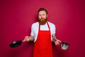 escéptico cocinero con barba y rojo delantal cocineros con pan y maceta foto