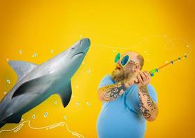 Fat afraid man with beard and sunglasses caught a shark with the fishing rod photo