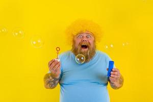 Amazed man with yellow wig in head play with bubbles soap photo