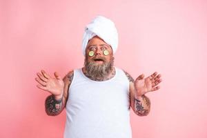 Amazed man with beard acts like a woman and has fun with a facial mask photo