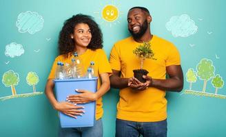 Happy couple hold a plastic container with bottles and a small tree over a light blue color. Concept of ecology, conservation, recycling and sustainability photo