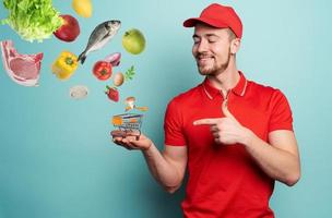 Deliveryman holds a small cart that is filled with food. Cyan background photo