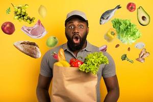 Deliveryman with wondered expression ready to deliver bag with food. Yellow background. photo