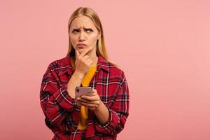 Blonde girl thinks about the right option. Yes or no. Confused and pensive expression. Pink background photo