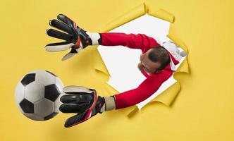 Goalkeeper exits from a hole and tries to tatches the ball. yellow background photo