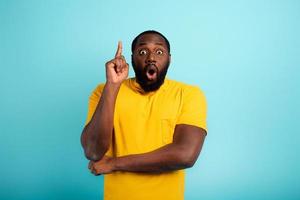 Boy indicates a above. amazed and shocked expression. cyan background photo