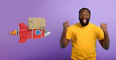 Black man is happy to receive a package. Concept of fast delivery like a rocket. Purple background photo