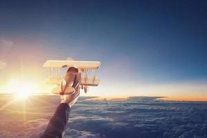 Close up of a vintage wooden toy airplane, held up by one hand, flying above the clouds in the sky photo