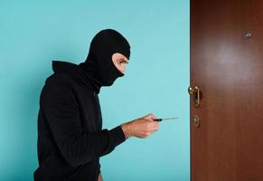 Thief with balaclava tries to open the door of apartment with a key photo