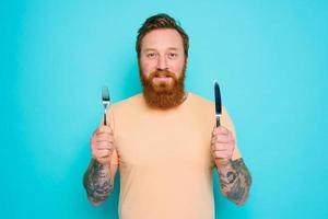 Man with tattoos is ready to eat with cutlery in hand photo