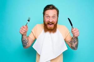 Hungry man with tattoos is ready to eat with cutlery in hand photo