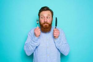 Man with tattoos is ready to eat with cutlery in hand photo