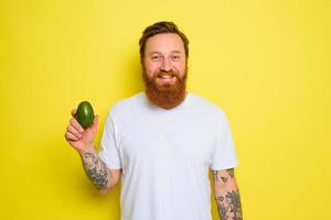 Happy man with beard and tattoos holds an avocado photo