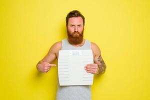 infeliz hombre con barba y tatuajes sostiene un electrónico equilibrar foto