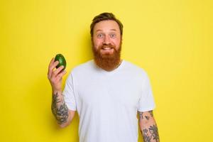 Happy man with beard and tattoos holds an avocado photo
