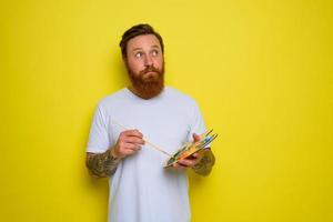 Undecided man with beard and tattoo is ready to draw with brushes photo