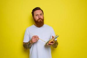 Man with beard and tattoo is ready to draw with brushes photo