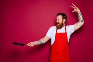 angry chef with beard and red apron cooks with pan photo