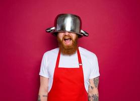 Happy chef with beard and red apron plays with pot photo