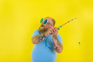 Fat man with beard and sunglasses have fun with the fishing rod photo