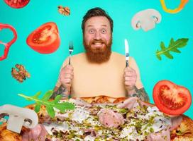 hombre con barba y tatuajes es Listo a comer un grande Pizza foto