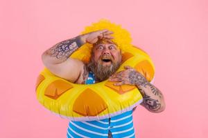 Fat amazed man with wig in head is ready to swim with a donut lifesaver photo