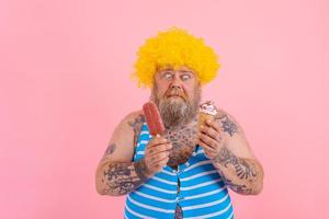 Fat man with beard and wig eats a popsicle and an icecream photo