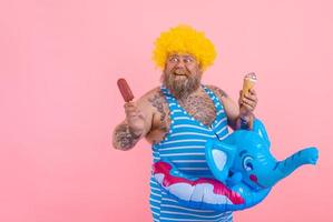 Fat man with beard and wig eats a popsicle and an icecream photo