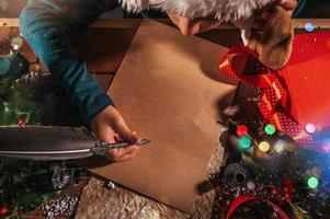 Child with christmas hat writes a letter to santa claus for gifts photo