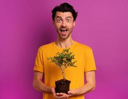 contento chico sostiene un pequeño árbol Listo a ser plantado terminado un ligero color. concepto de forestación, ecología y conservación foto