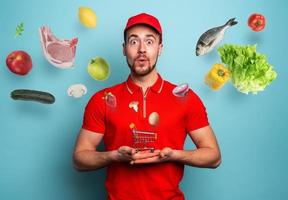 Deliveryman holds a small cart that is filled with food. Cyan background photo