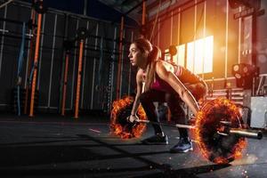 Athletic girl works out at the gym with a fiery barbell photo