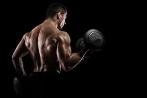 Athletic man training biceps on black background photo