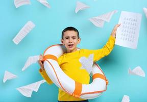 Young boy student is drowning in a sea of sheets of exercises. Cyan background photo