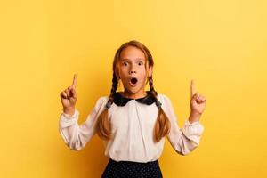 Young student is with shocked expression and indicates something. Yellow background photo