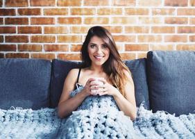 Brunette girl drinking cappuccino for breakfast on a sofa. Concept of relax. photo