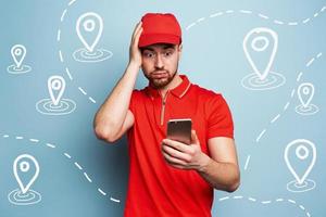 Confused courier man watches his smartphone due to a lot of packages to delivery photo