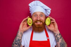 happy chef with beard and red apron holds an avocado photo