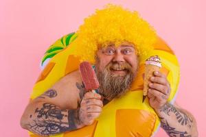 Fat man with beard and wig eats a popsicle and an icecream photo