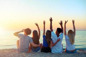 grupo de contento amigos teniendo divertido a Oceano playa a amanecer foto