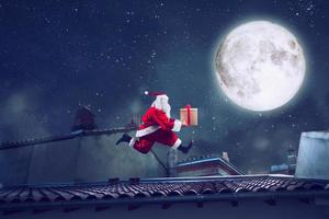 Santa Claus runs fast on a roof with a present photo