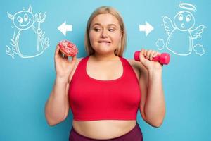 grasa niña piensa a comer rosquillas en lugar de lo hace gimnasia. concepto de indecisión y duda con ángel y diablo sugerencia foto