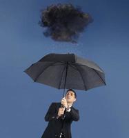 empresario con paraguas y un negro nube con lluvia. concepto de crisis y financiero problema foto