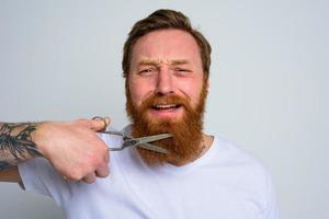 Unhappy man with scissors doees not want to cut the beard photo