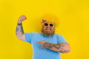 Fat man with wig in head and sunglasses shows his muscle photo