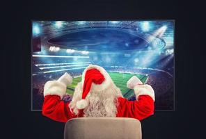 Joyful Santa Claus, soccer fan, watches a game on television photo